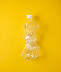 Minimalistic ecological concept. Crumpled plastic bottle on yellow background. Environmental plastic pollution