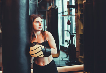 Fototapeta na wymiar A tired young sport woman in boxing gloves resting after heavy boxing training with punching bag.