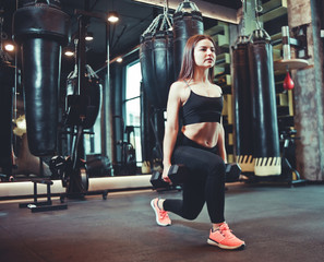 Training legs at the gym. Attractive fit woman doing lunges with dumbbells.