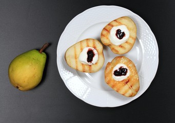 Grilled pears with whipped cream and jam.  Grilled fruit on the plate and black background.