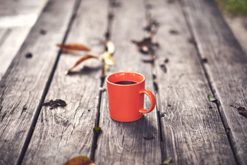 An orange mug filled with black coffee sitting on a rustic table
