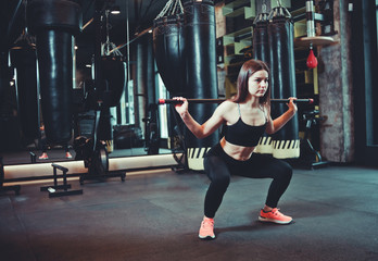 Beautiful fit woman doing squats exercise with gymnastic stick at boxing gym