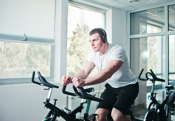 Healthy lifestyle concept. Young sporty man in white t-shirt and shorts is exercising bike at spinning class . Cardio training