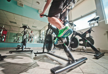 Fototapeta na wymiar Wide angle view of man in sports sneakers and shorts does exercises on cardio bike at spinning class. Healthy lifestyle concept
