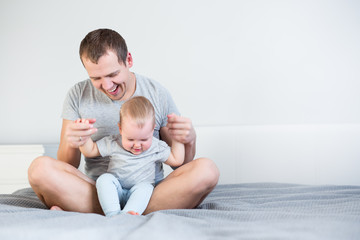 father and little cute daughter having fun together sitting on the bed and copy space over white wall