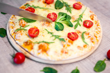 close up of big knife cutting pizza with tomatoes and herbs over wooden table