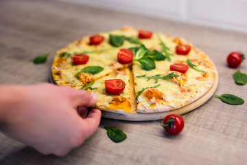 male hand picking slice of tasty pizza with tomatoes and herbs over wooden table