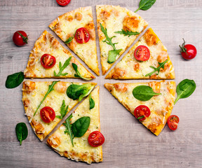 tasty sliced pizza with tomatoes and herbs without one slice over wooden table background