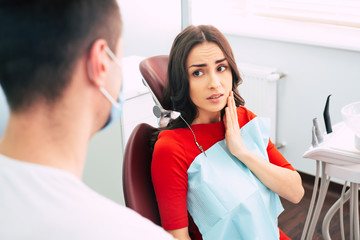 I’ve got a toothache! Worried looking girl in the dentist chair in front of the doctor is...