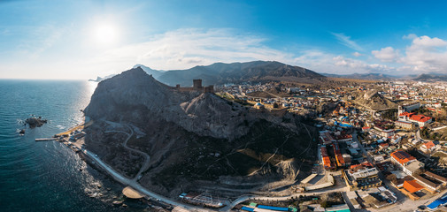 Obraz premium Genoese fortress in Sudak, Crimea. Aerial panorama view of ruins of ancient historic castle on crest of mountain near sea and small town at foot of rocks. Beautiful summer tourist landscape