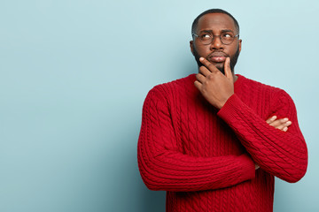 Human facial expressions concept. Contemplative dark skinned guy rubs chin as thinks, makes...