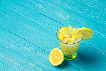 Water with lemon. Lemonade with lemon slices on blue wooden background.