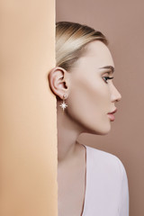 Earrings and jewelry in ear of a sexy blonde woman pressed against the paper beige. Perfect blonde...
