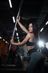 Girl posing in the gym, showing off her body, holding a barbell