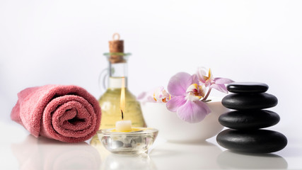 Spa still life composition on white background. Zen spa stones next to towel, burning candle, bottle with oil and bow with flower.