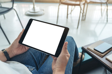Mockup image of a woman sitting and holding black tablet pc with blank white desktop screen horizontally