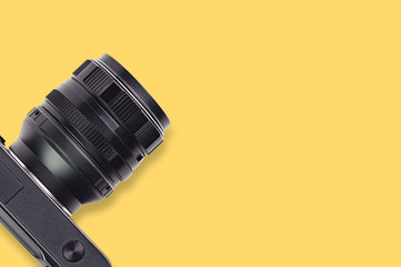 One professional digital black camera with lens on yellow table. Copy space for your text. Top view. Travel or video blogging concept