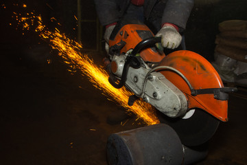 Closeup Worker saws metal with a large circular saw in the hands of the factory workshop, sparks