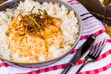 A bowl of honey mustard chicken served with white rice and almond flakes, presented on a wooden board