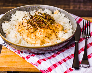 A bowl of honey mustard chicken served with white rice and almond flakes, presented on a wooden board