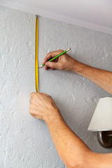 Hands make wall marking with tape measure and pencil