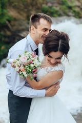 Beautiful portrait of happy bride and groom in nature on waterfall background