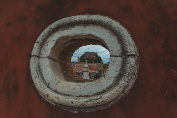 Hole in a wall with the entrance to the old Venetian fortress of Corfu in the background