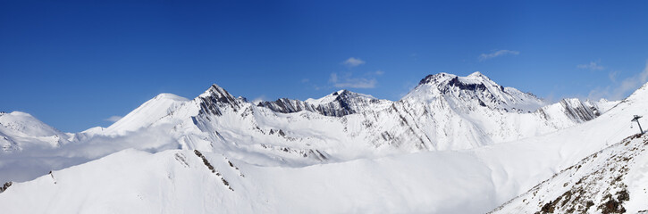 Panorama of mountains with snowy off-piste slope and blue sunlit sky at winter