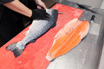 Closeup fresh salmon fish preparing fillet with knife on red cutting board in professional kitchen of restaurant. Concept Japanese food, sushi, sashimi, semi finished product, norwegian fish soup