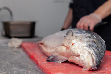 Closeup whole fresh salmon fish preparing fillet with knife on red cutting board in professional kitchen of restaurant. Concept Japanese food, sushi, sashimi, semi finished product, norwegian soup