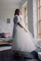 Portrait of a beautiful blonde bride in the interior. Morning young bride in a bathrobe. Wedding photography. Smiling and cute girl stands near the window.