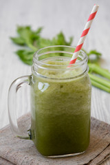 Green celery smoothie in glass jar over white wooden surface, side view. Close-up.