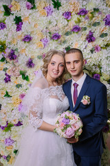 beautiful bride and groom on the background of a wall of flowers.