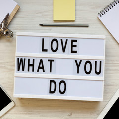 'Love what you do' words on lightbox, tablet, smartphone, notepad and pencil over white wooden surface, top view. Business concept. From above, flat lay, overhead.