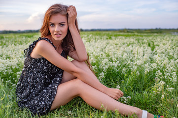 Naklejka na ściany i meble Young lady sitting outdoors in a field of white flowers.