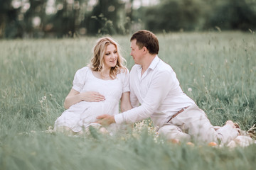 beautiful pregnant woman with her husband sitting on lawn in summer day.