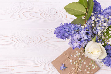 A gift box wrapped in craft paper and blue hyacinth flowers, white roses on a white table top. Flat lay. Copy space for text