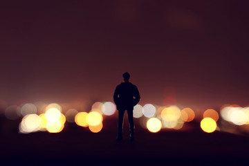 Silhouette of miniature man looking at the city lights in the nigh