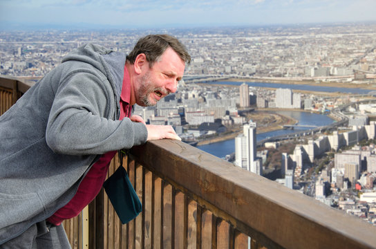 Mature man suffers from acrophobia. He is scared on the viewing platform above a megalopolis.