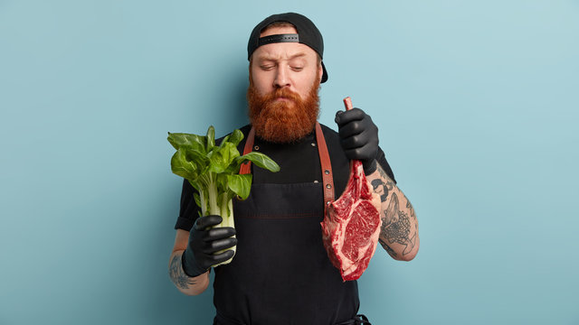 Indoor shot of male cook holds green bok choy in one hand and raw meat in other, going to bake pork, prepare fresh salad, cooks during working time, models over blue background. Nutrition concept