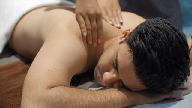 Medium shot of Asian man lying on spa bed and receiving back massage