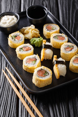 sushi roll in the omelette with rice, cheese, salmon and avocado closeup served with sauces, wasabi and ginger on a plate. vertical