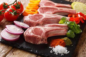 Raw lamb steaks on the bone surrounded by vegetable ingredients close-up. horizontal