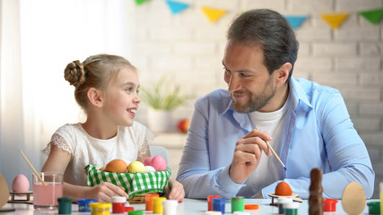 Father and daughter smiling, painting eggs for Easter party, family relationship
