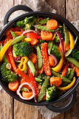 Delicious vegetarian vegetable stir fry with sesame close-up in a bowl, Vertical top view