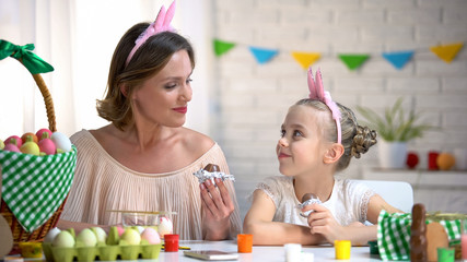 Beautiful mother and daughter in funny headbands eating Easter chocolate eggs