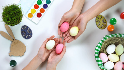Dyed eggs in female hands, Easter bunny decoration and holiday basket on table