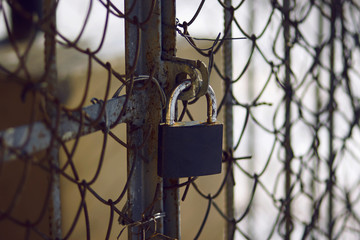 Old, scratched and rusty from time to time padlock closes the metal gate with a mesh fence