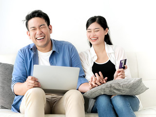 Happy Asian couple shopping online with holding credit card and laptop and sitting at home together, lifestyle concept.