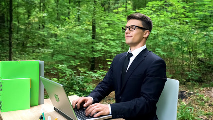 Business man breathing fresh air in eco-friendly office, sitting at desk in park